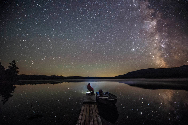 A camper takes in the night air and sky from the end of the lone dock on the remote Rock Pond in the Unorganized Territories of the northwest mountains in Maine on Aug. 15, 2020.